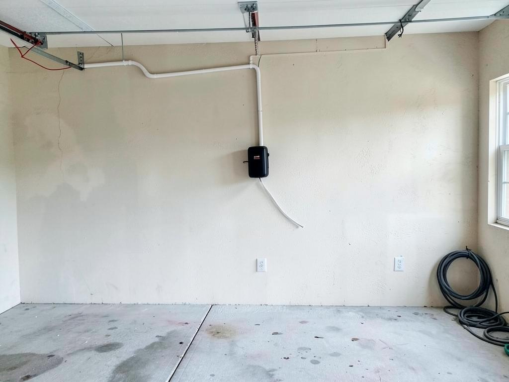 Black EV charger on the far garage wall with conduit along the ceiling line